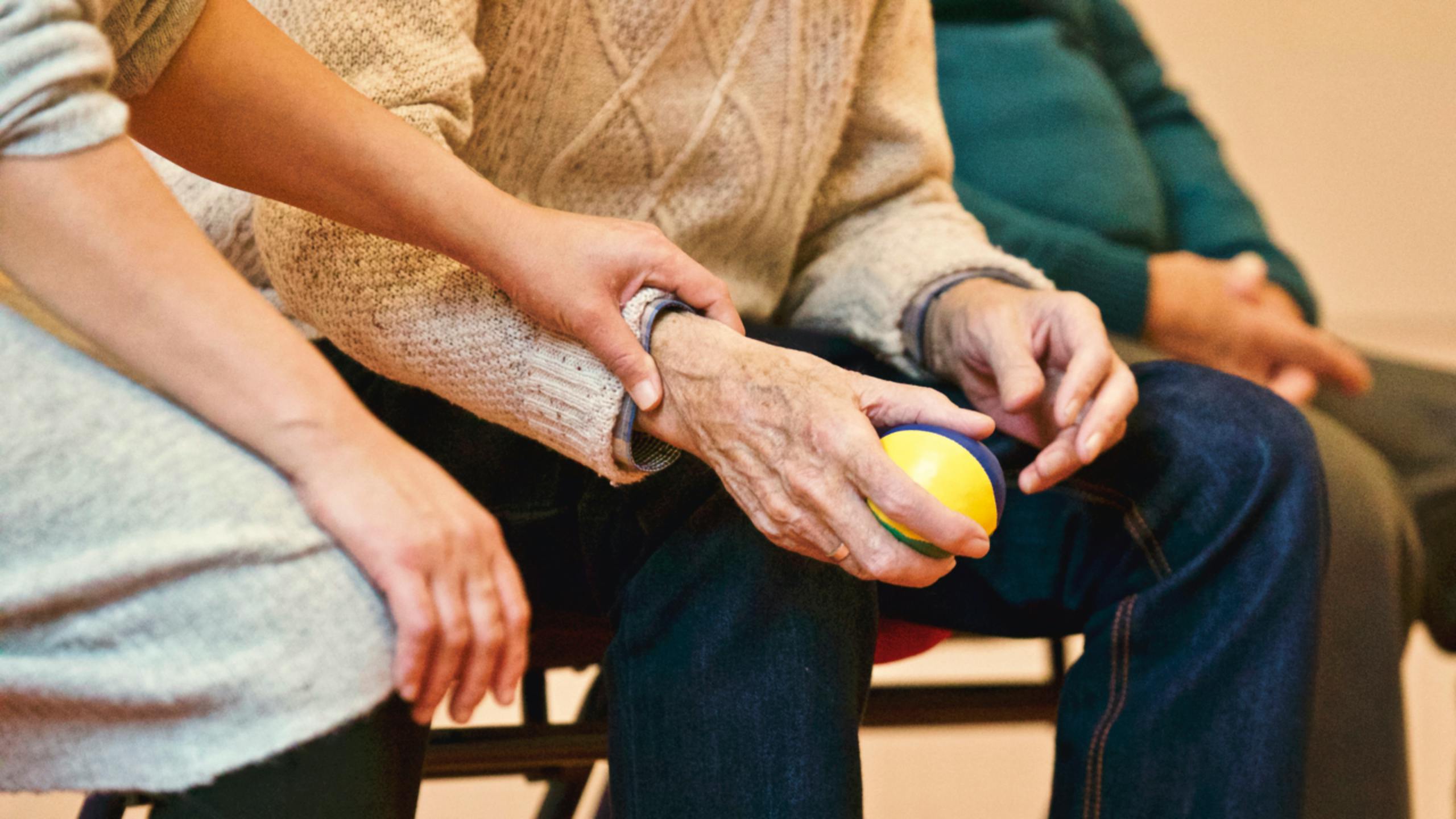 Ein Mann wird in einem Pflegeheim betreut. Er hält einen Ball in der Hand