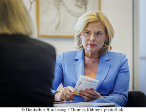 Bundestagspräsidentin Julia Klöckner sitzt an einem Tisch. In der Hand hält sie verschiedene Unterlagen. Sie ist in ein blaues Akko gekleidet. Darunter trägt sie eine weiße Bluse.
