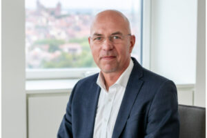 Maik Render, Sprecher des Vorstandes der N-ERGIE in Nürnberg in einem Büro. Er trägt eine Brille sowie einen schwarzen Anzug unter dem er ein Hemd anhat.